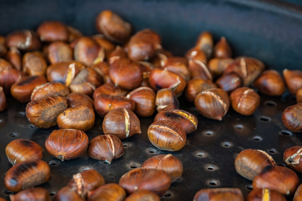 Viele Maronen liegen angeritzt in einer dunklen Röstpfanne.