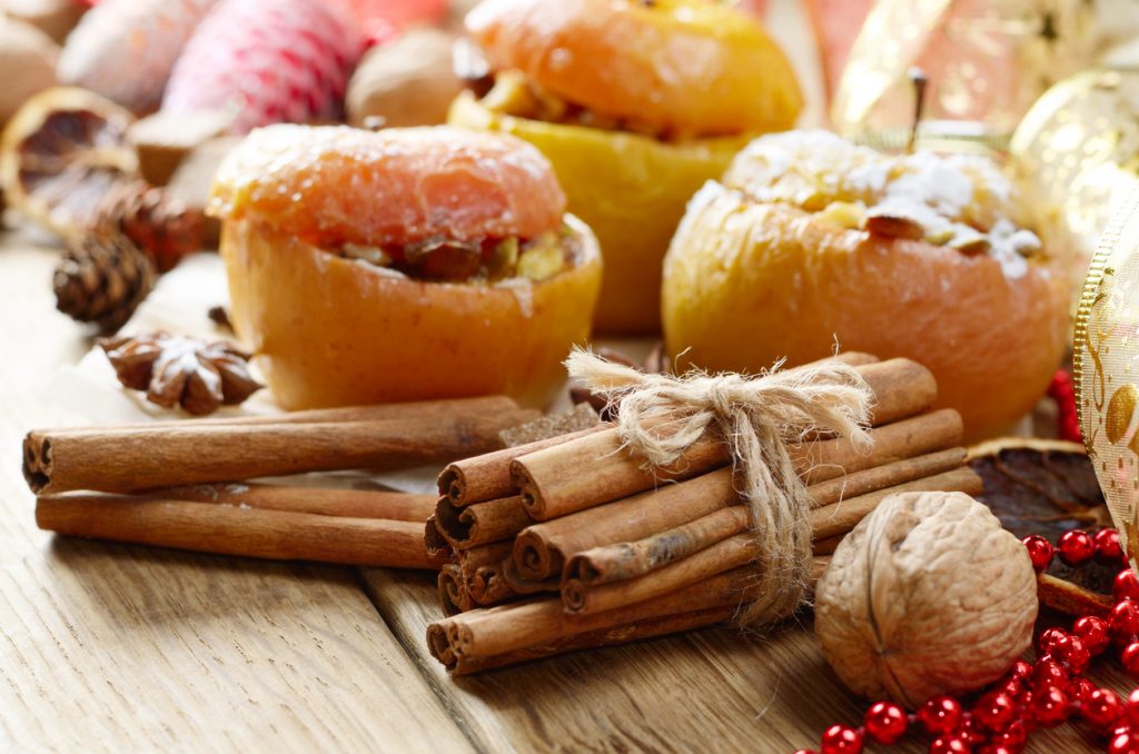 Zimtstangen, Nüsse und gefüllte Äpfel auf einem Holztisch im Weihnachtsstil.