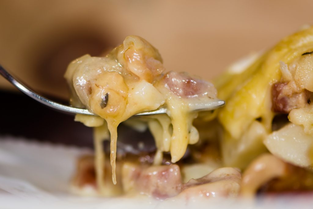 Ein Löffel hebt ein Stück Tartiflette mit geschmolzenem Käse, Kartoffeln und Speck an.