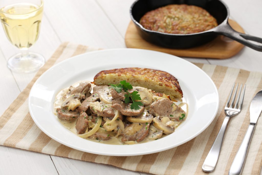 Züricher Kalbsragout wird auf einem Teller mit Rösti serviert und mit Petersilie garniert.