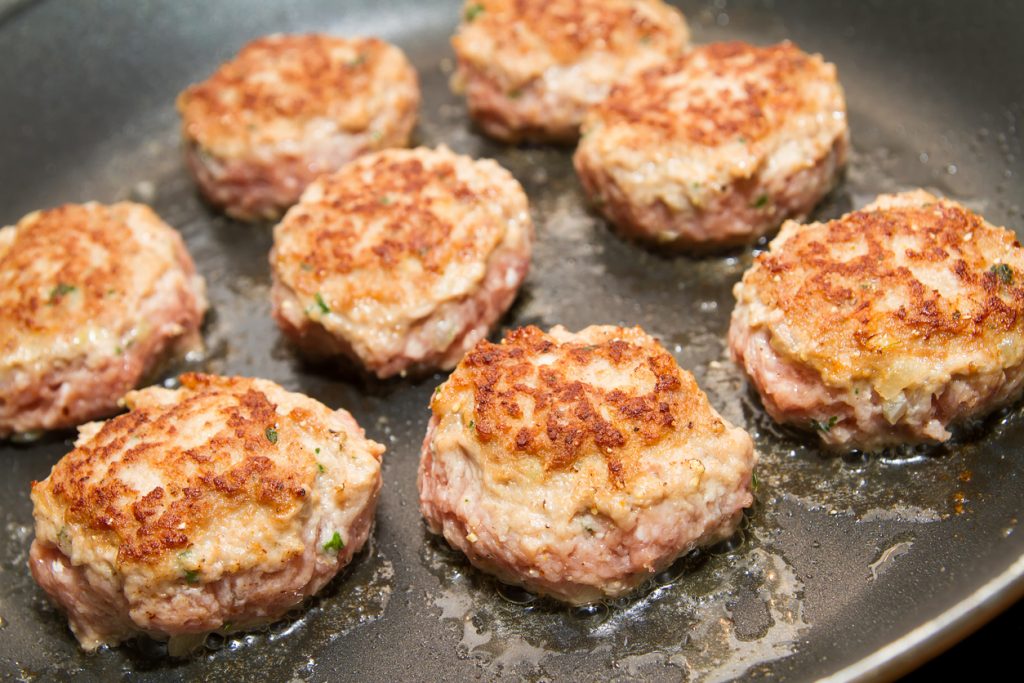 Mehrere frisch angebratene Bouletten liegen in einer heißen Pfanne und brutzeln im Fett.