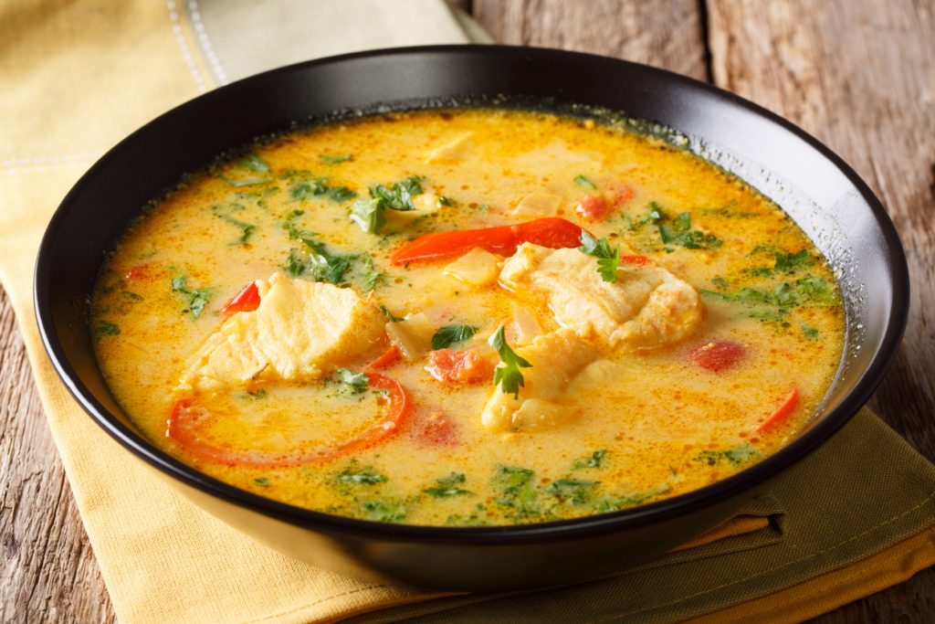Moqueca mit Fisch, Paprika und Kräutern liegt in einer cremigen Sauce in einer schwarzen Schale.