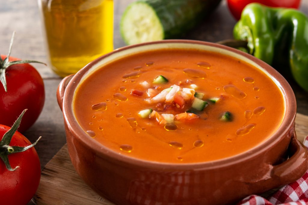 Nahaufnahme einer Schale Gazpacho mit gewürfeltem Gemüse als Topping und feinen Öltropfen auf der Oberfläche.