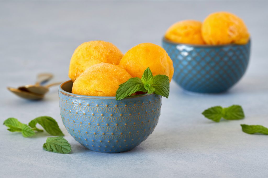 Mehrere Kugeln Mangoeis liegen in einer blauen Schale, dekoriert mit Minze.