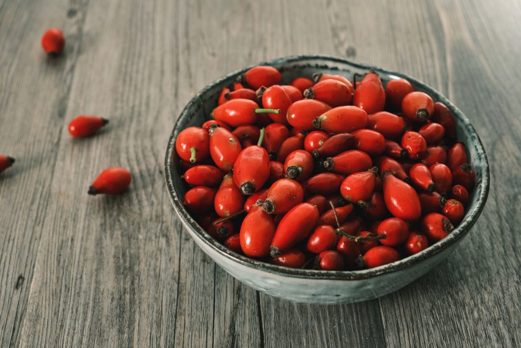 Eine Schale voller roter Hagebutten steht auf einem Holztisch.