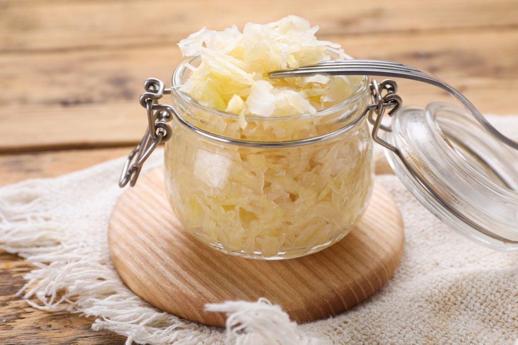 Aus einem geöffneten Bügelglas wird Sauerkraut mit einer Gabel herausgenommen.