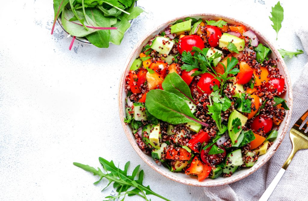 Eine Schüssel mit Quinoa-Salat, Gemüse und Kräutern steht auf hellem Untergrund.