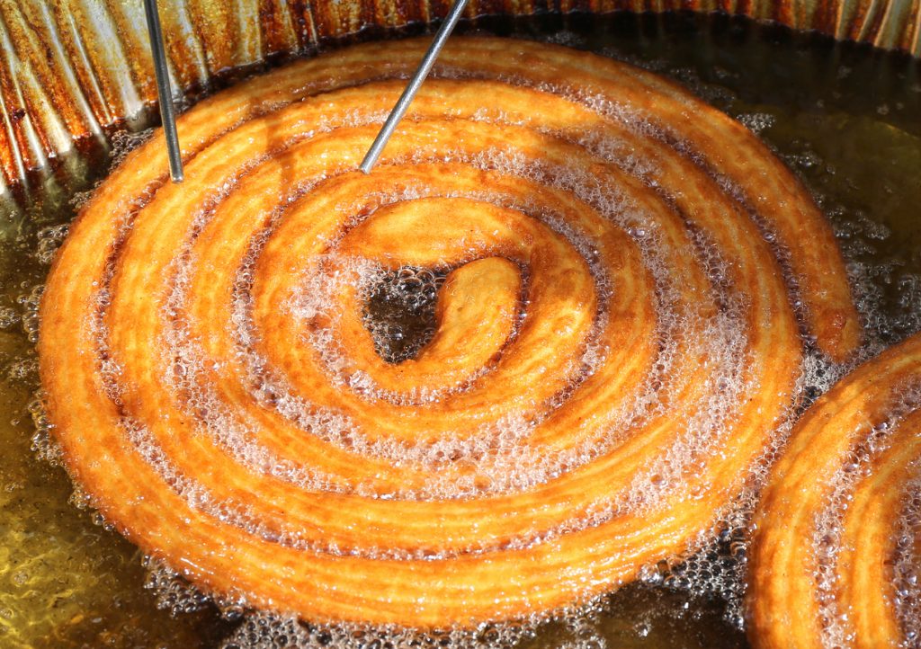 Große Churros Spirale frittiert in heißem Öl mit aufsteigenden Blasen.