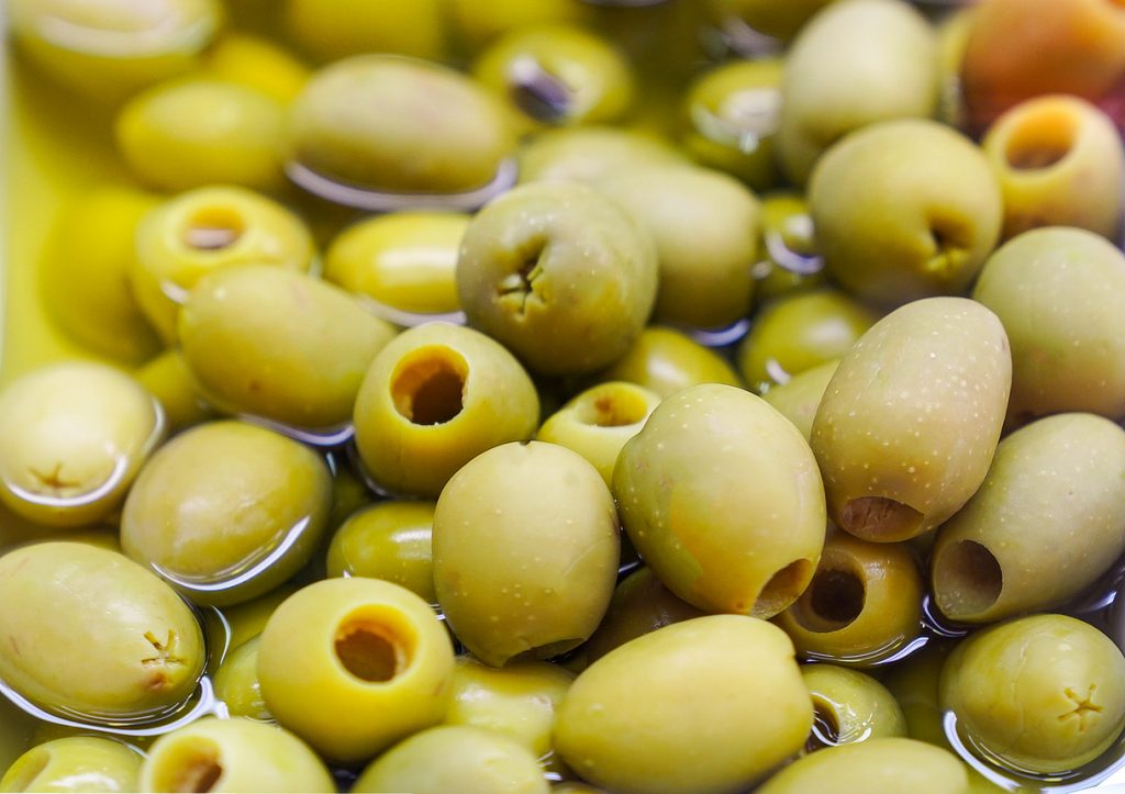Nahaufnahme von grünen, entsteinten Oliven in einer Flüssigkeit.