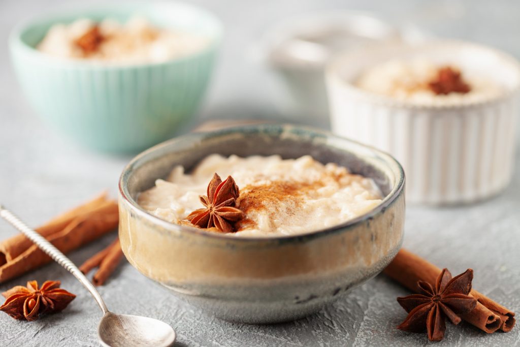 Eine Schale Arroz con Leche ist mit Zimt bestäubt und mit Sternanis dekoriert, daneben liegen Zimtstangen.