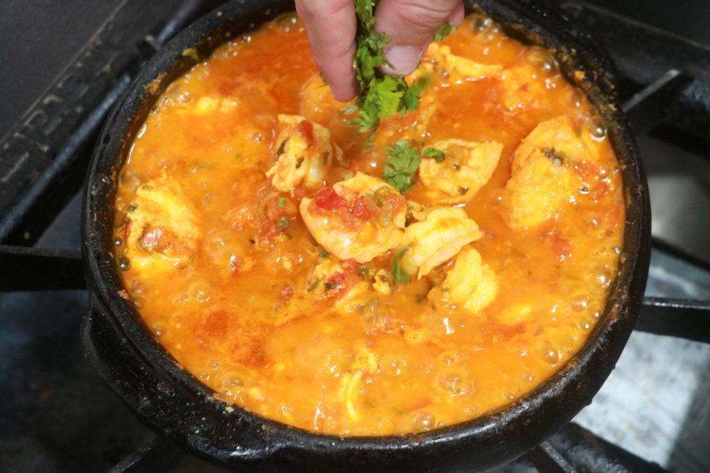 Eine Moqueca in orangefarbener Sauce wird im Tontopf mit Kräutern bestreut.