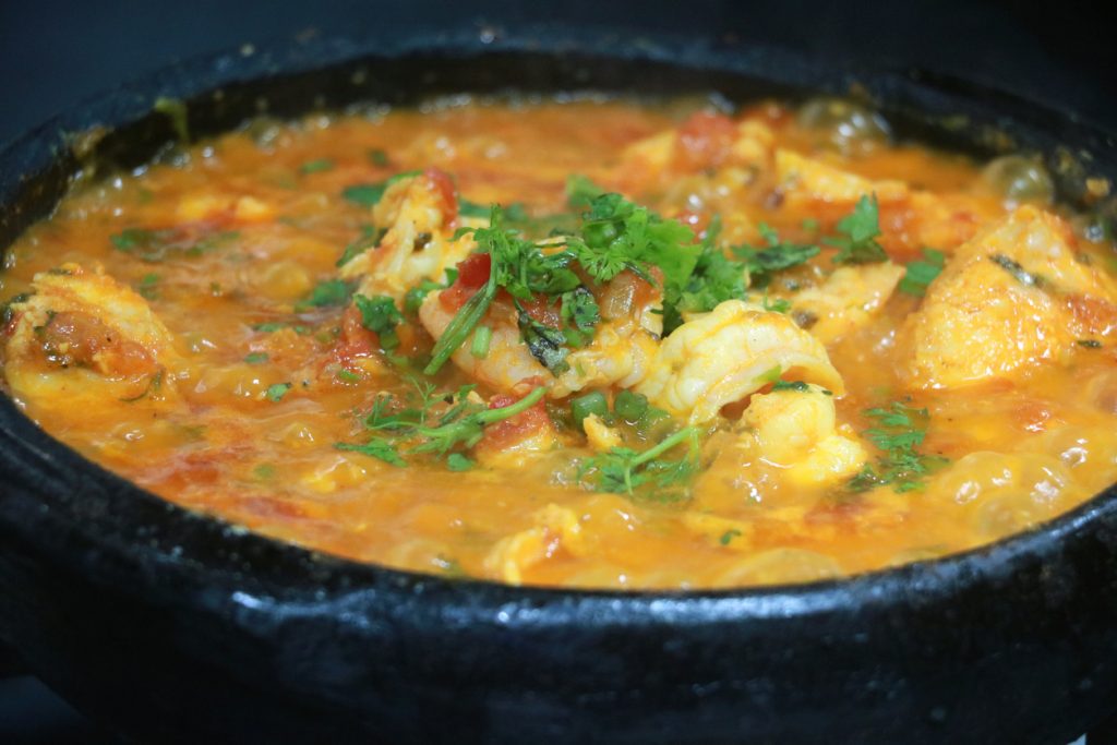 Moqueca in einem schwarzen Tontopf ist in orangefarbener Sauce gekocht und mit Kräutern bestreut.