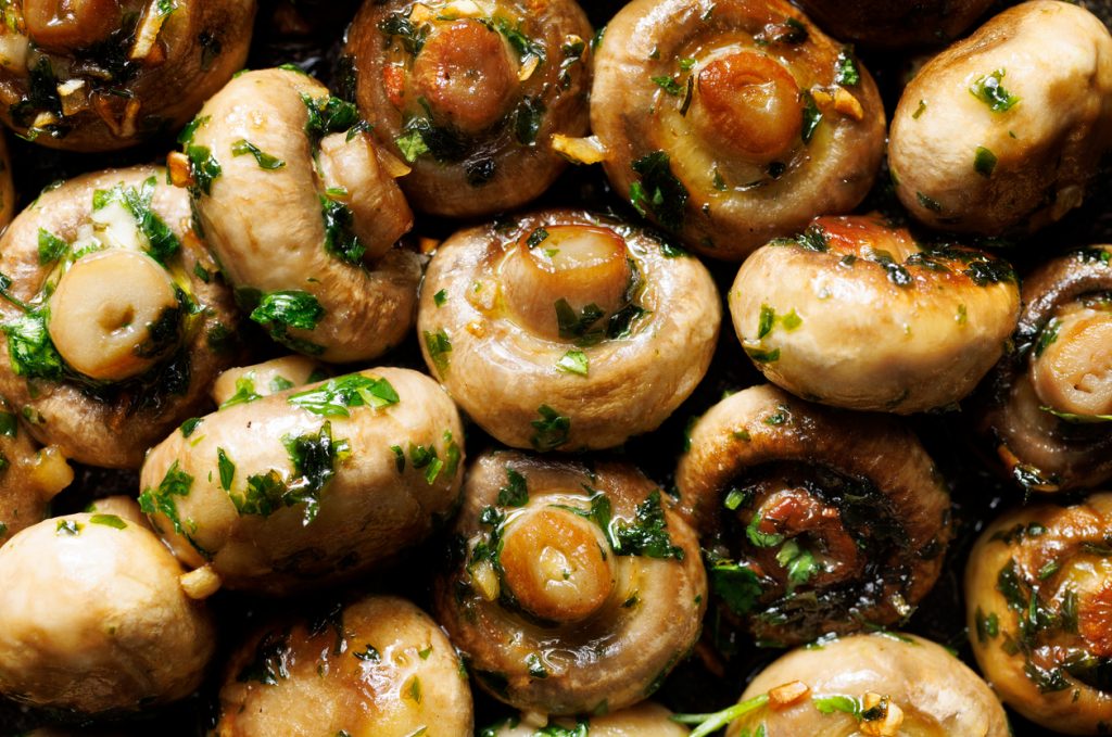 Gebratene Champignons mit Knoblauch und Petersilie in Öl als Nahaufnahme.