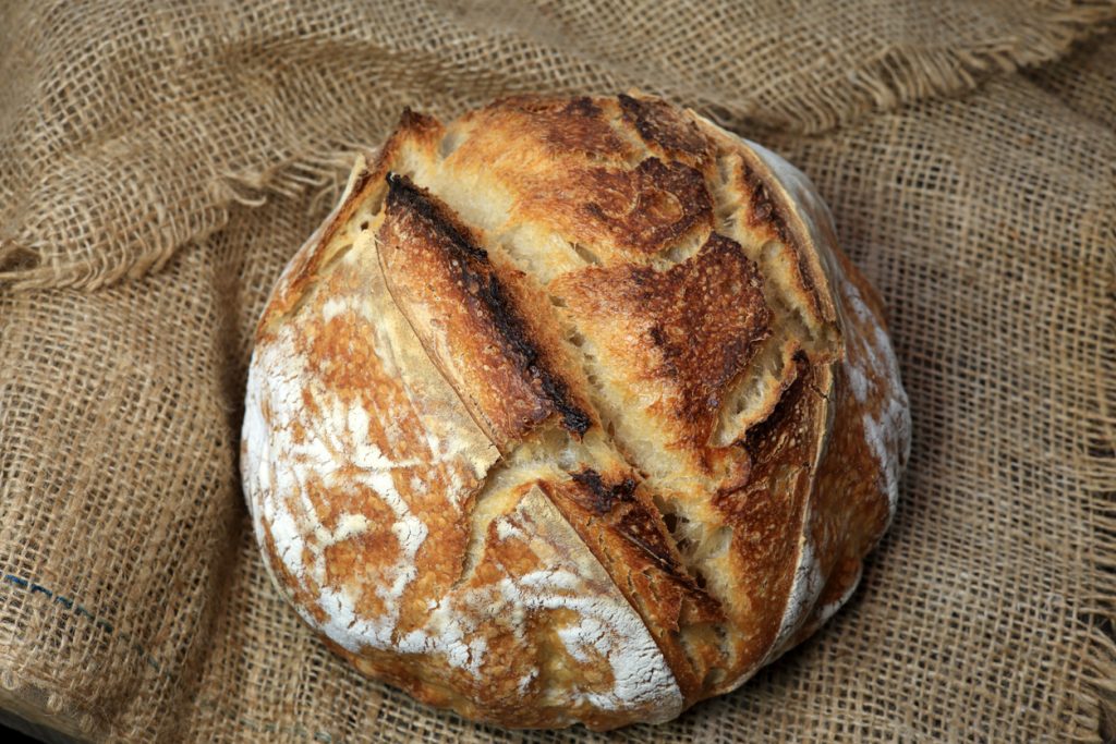 Ein rundes Sauerteigbrot mit bemehlter Kruste liegt auf grobem Jutestoff.