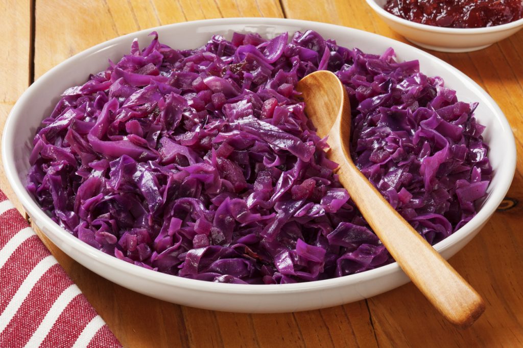 Eine Schüssel mit gegartem Rotkohl steht auf einem Holztisch und ein Holzlöffel liegt darin.