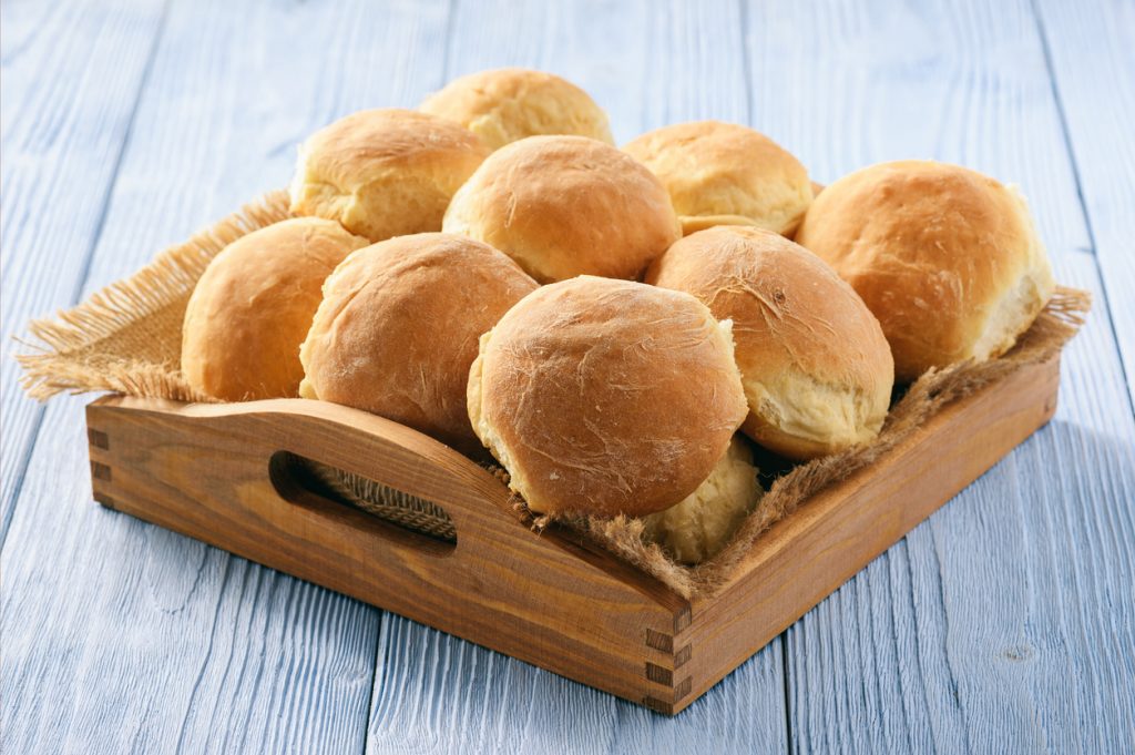 Kartoffelbrötchen liegen goldbraun gebacken in einem Holztablett auf hellblauem Holztisch.