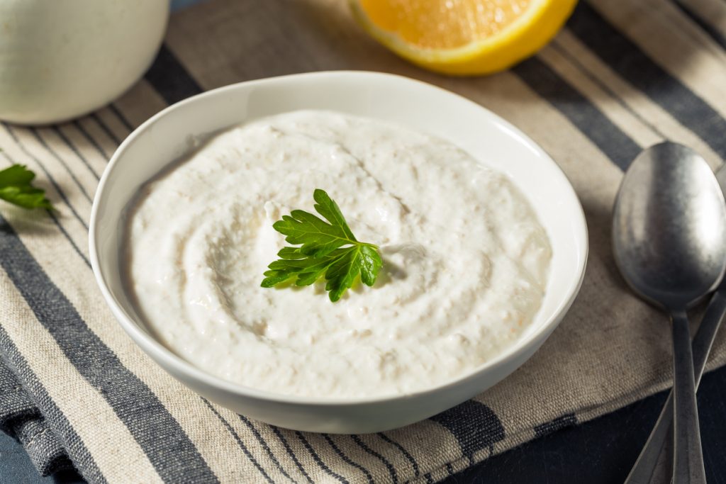 Eine Schale Meerrettichsauce ist mit Petersilie garniert und steht neben Zitrone und Löffel.