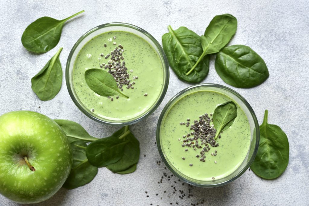 Zwei Gläser Apfel-Spinat-Smoothie sind von oben fotografiert und mit Chiasamen und Spinat dekoriert.