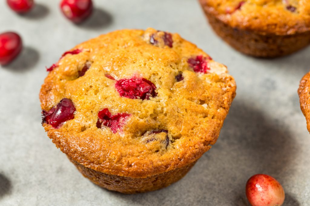 Ein goldbrauner Cranberry Muffin liegt nah aufgenommen auf einem Blech, umgeben von frischen Cranberries.