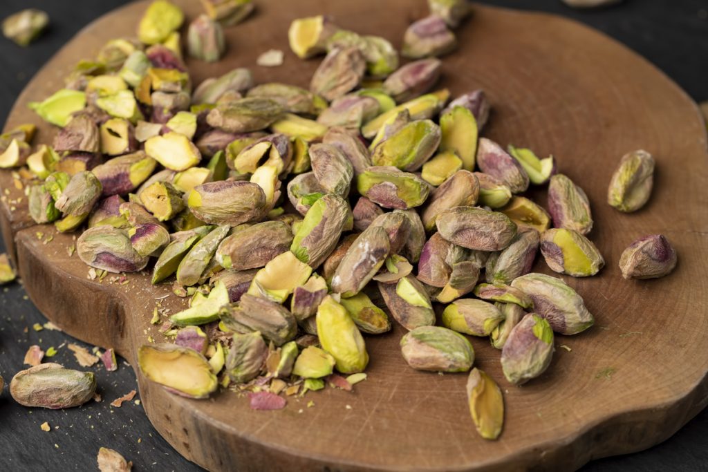 Geschälte Pistazienkerne sind auf einem runden Holzbrett verstreut.