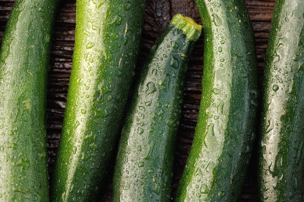 Mehrere grüne Zucchini liegen dicht nebeneinander und sind mit Wassertropfen bedeckt.