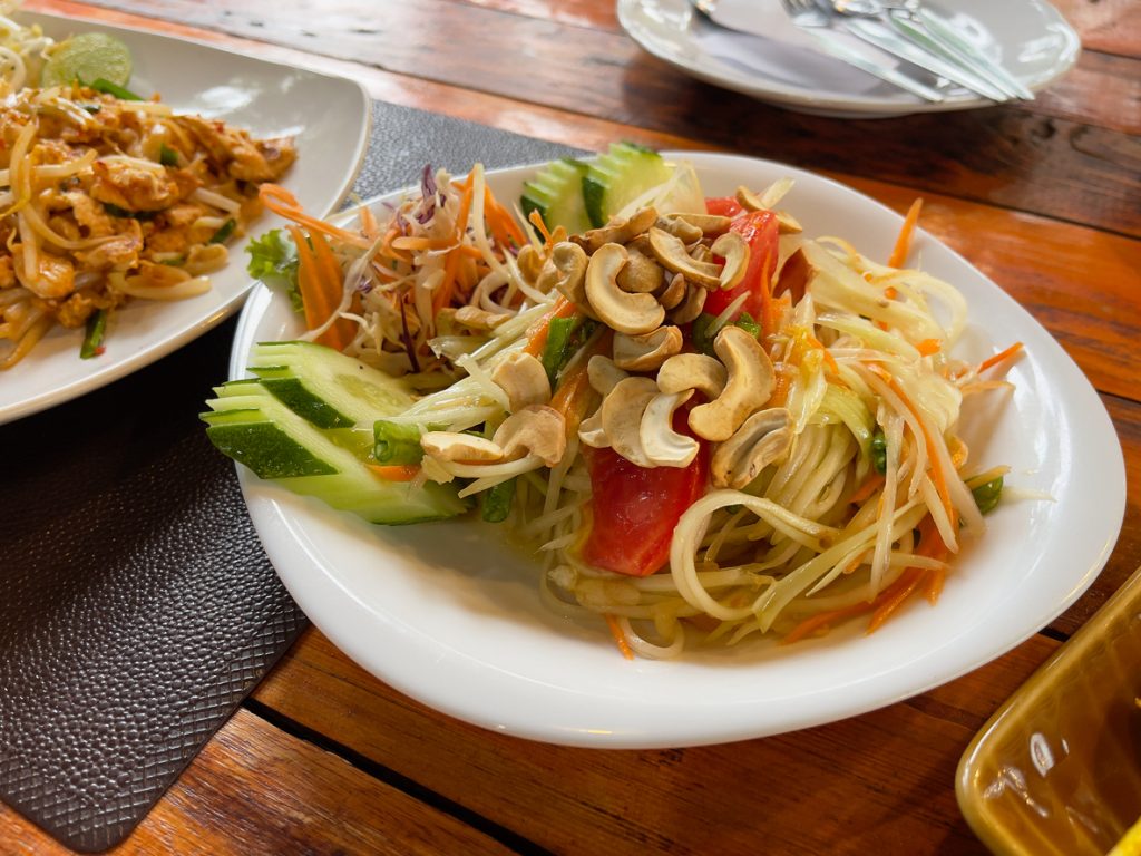 Ein Teller Som Tam Thai ist mit Papayastreifen, Gemüse und Cashews auf einem Holztisch angerichtet.