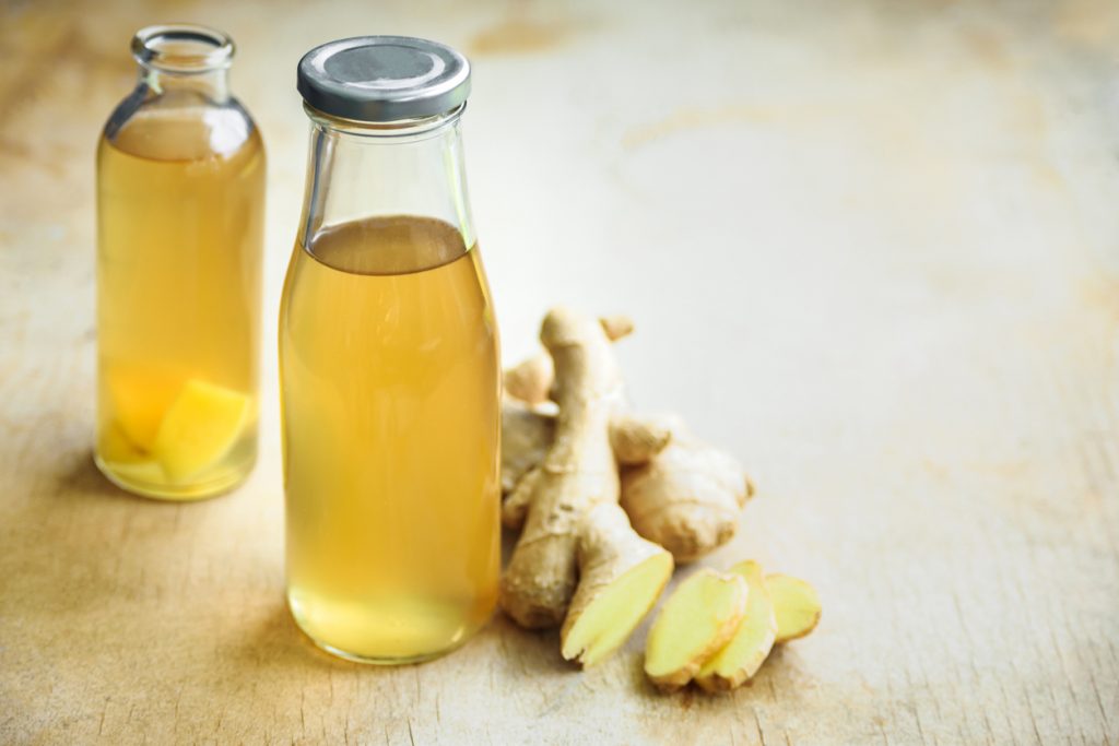 Ein Glas gefüllt mit Eiswürfeln, einer Zitronenscheibe und Mineralwasser, in das ein Schuss Goldene Ingwer-Essenz gegossen wird.