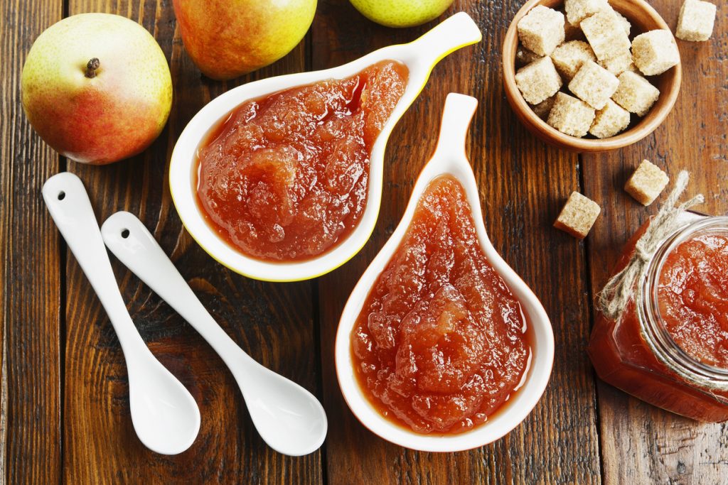 Zwei Schälchen Birnenmarmelade, dazu Birnen, Zuckerwürfel und ein Glas Marmelade auf Holz.