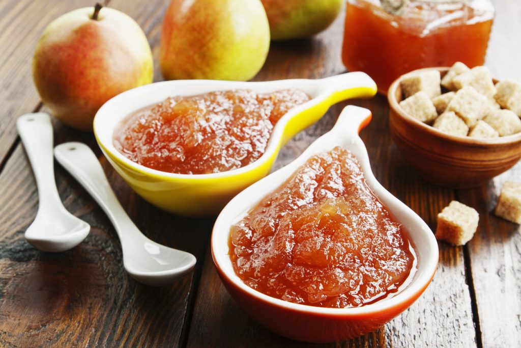 Zwei Schälchen mit Birnenmarmelade, dazu Birnen und Würfelzucker auf einem Holztisch.