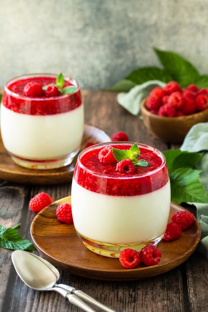 Hochkant-Aufnahme einer Panna Cotta in einem bauchigen Glas mit viel Fruchtsoße und Minze.