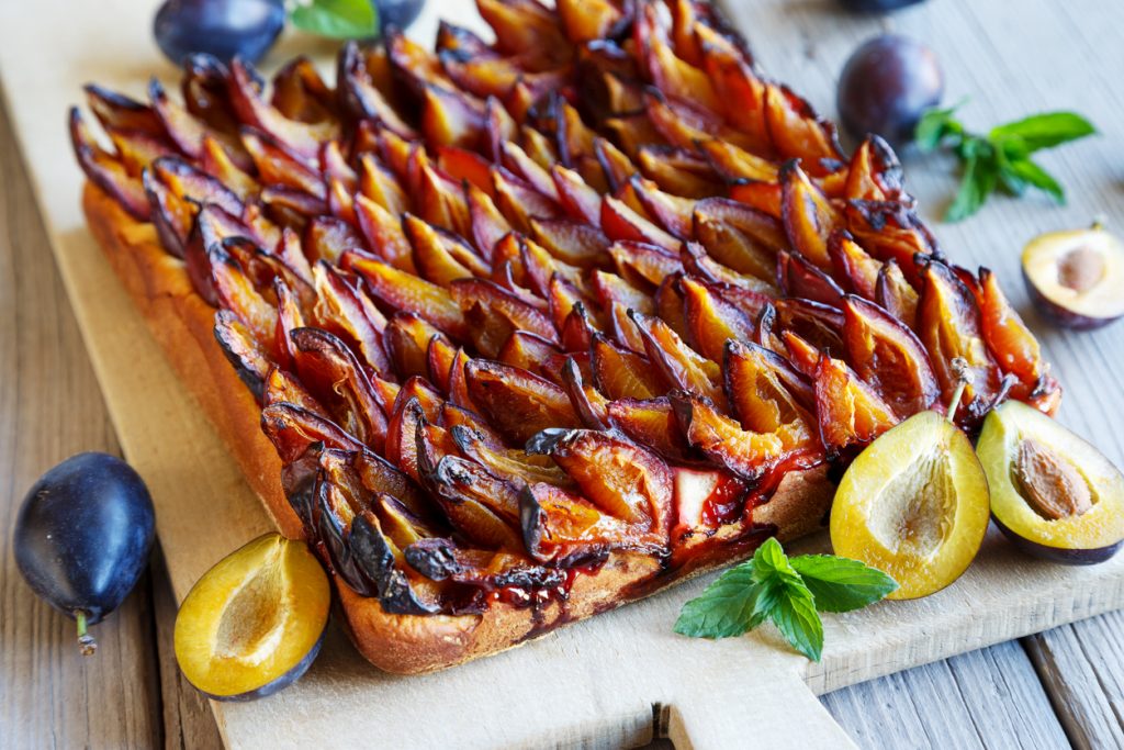 Ein ganzer Pflaumenhefekuchen liegt auf einem Holzbrett, dicht belegt mit gebackenen Pflaumen.