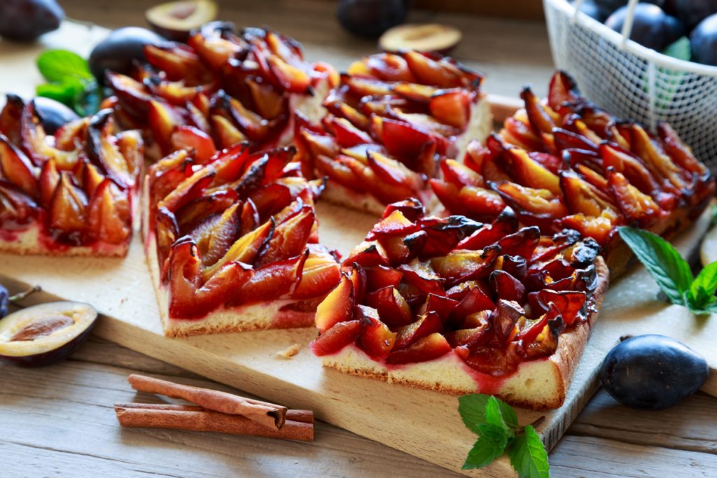 Mehrere Kuchenstücke aus Pflaumenhefekuchen liegen eng beieinander auf einem Brett.