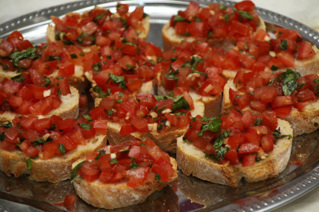 Viele Bruschetta-Scheiben sind auf einem Tablett angerichtet und mit Tomaten und Basilikum belegt.