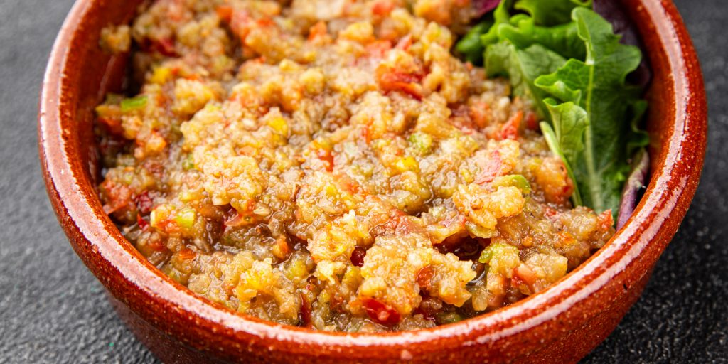 Ein Auberginen Dip füllt eine braune Schüssel und liegt neben frischen Salatblättern.