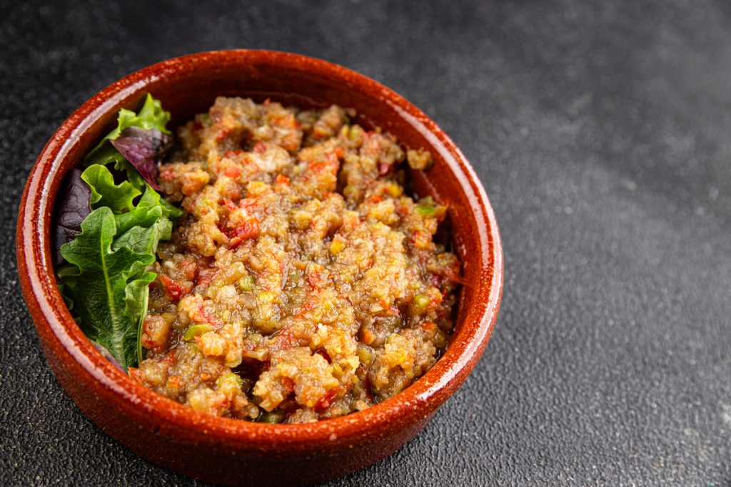 Ein cremiger Auberginen Dip liegt in einer braunen Schale und ist mit Salatblättern dekoriert.