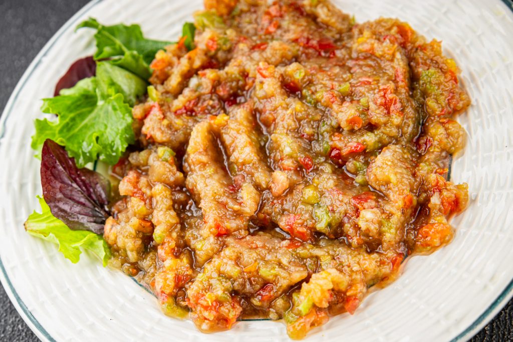 Auberginen Dip ist auf einem hellen Teller verteilt und wird mit grünen Salatblättern serviert.