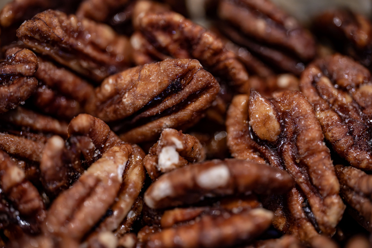 Eine extreme Makroaufnahme von Pecannüssen, die mit einer glänzenden, dunklen Zuckerschicht überzogen sind.