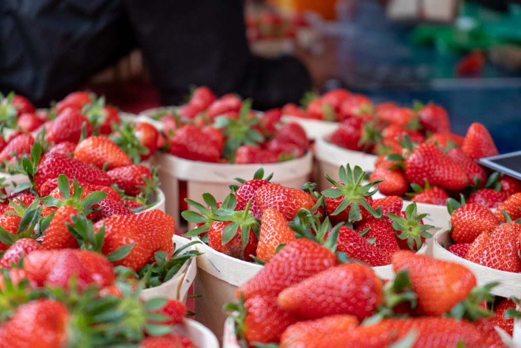 Zahlreiche kleine Holzkörbchen sind bis oben hin mit großen, glänzenden Erdbeeren gefüllt.