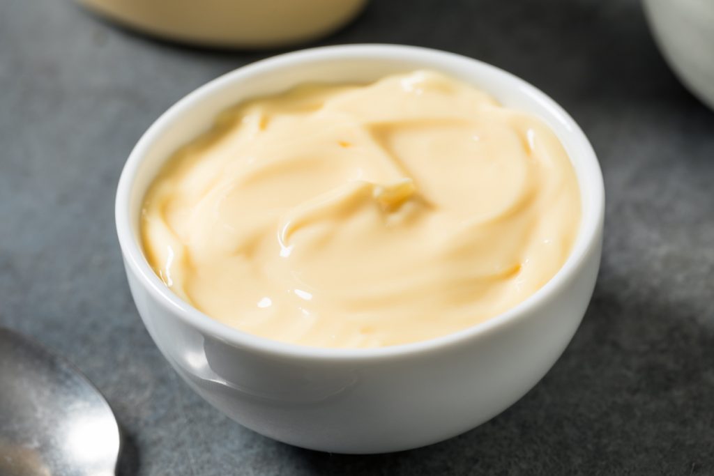 Eine weiße Porzellanschale ist randvoll mit glatter, hellgelber Mayonnaise gefüllt.