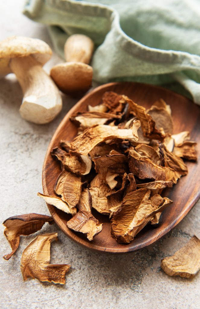 Eine braune Holzschale gefüllt mit getrockneten Steinpilzscheiben auf einem rustikalen Hintergrund.