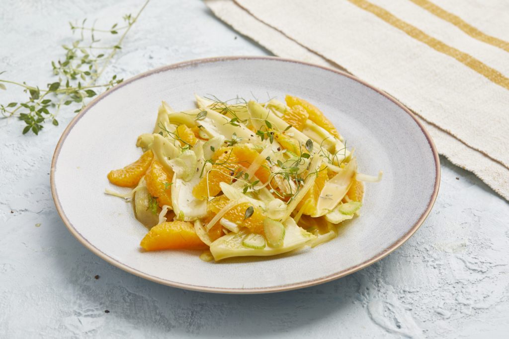 Fenchel-Orangen-Salat ist auf einem grauen Teller angerichtet und mit Kräutern und Fenchelgrün bestreut.
