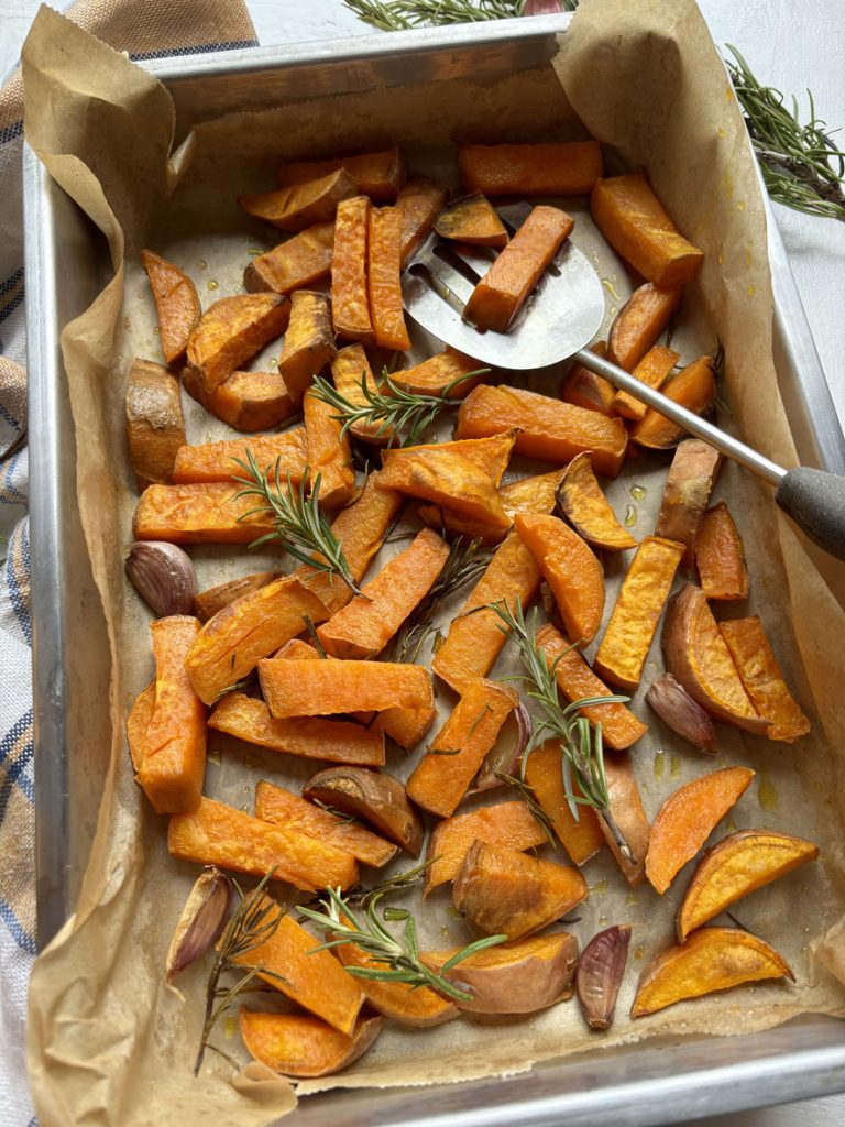 Ein Pfannenwender hebt eine Portion gebackener Süßkartoffeln von einem Backblech.