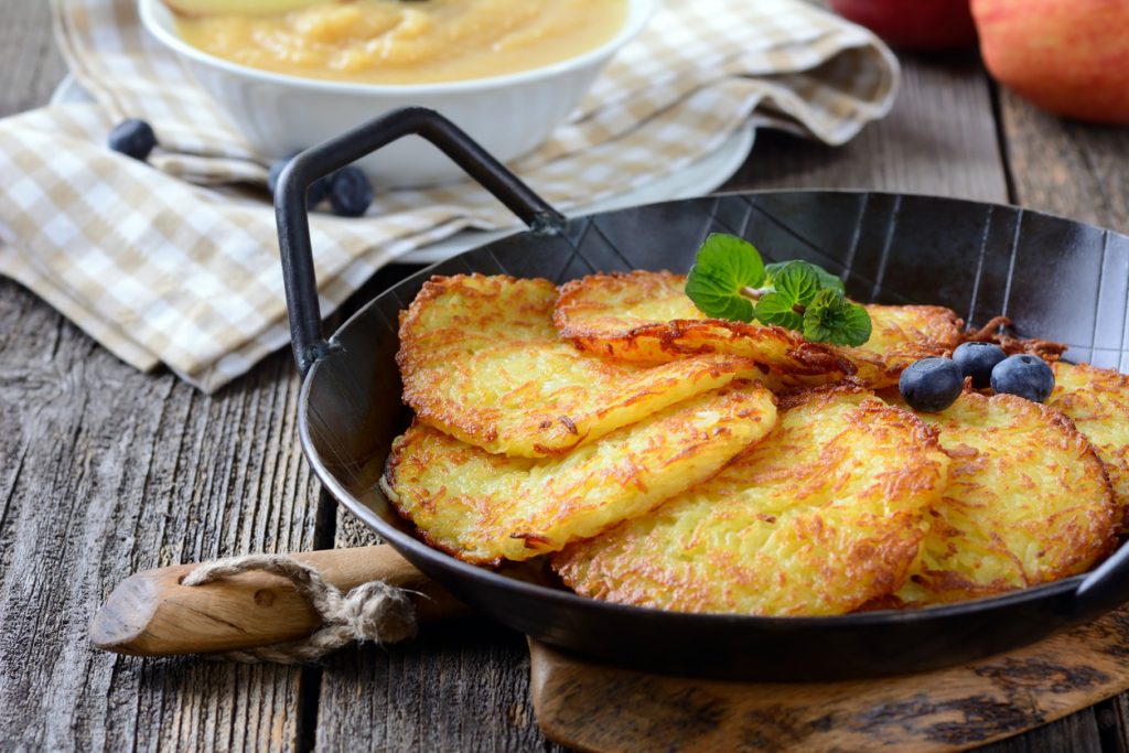 Goldbraune Kartoffelpuffer liegen in einer Pfanne und werden mit Minze, Beeren und Apfelmus serviert.