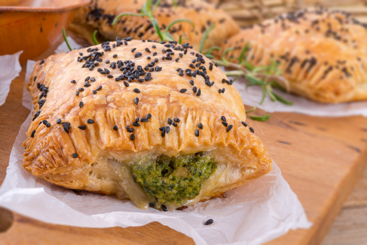 Eine Nahaufnahme einer einzelnen Blätterteigtasche, bei der die würzige Spinatfüllung deutlich im Anschnitt zu sehen ist.