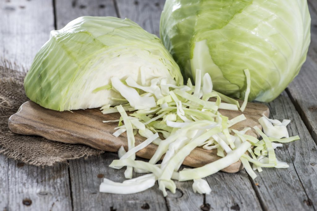 Ein halbierter Weißkohlkopf liegt auf einer dunklen Holzoberfläche; die eng aneinanderliegenden, hellen Blattschichten sind deutlich zu erkennen.