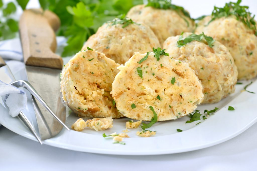 Mehrere klassische Semmelknödel liegen auf einem weißen Teller und sind mit Petersilie bestreut.