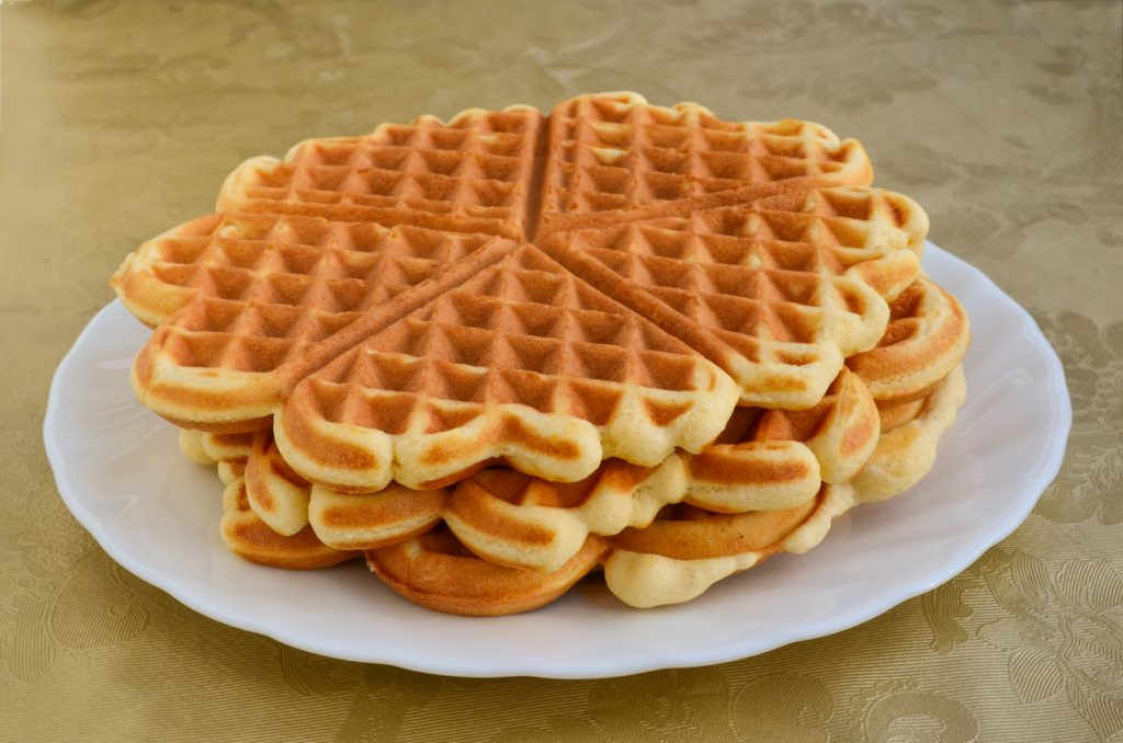 Drei perfekt gebackene Waffeln in Blumenform sind dekorativ auf einem weißen Teller angerichtet.