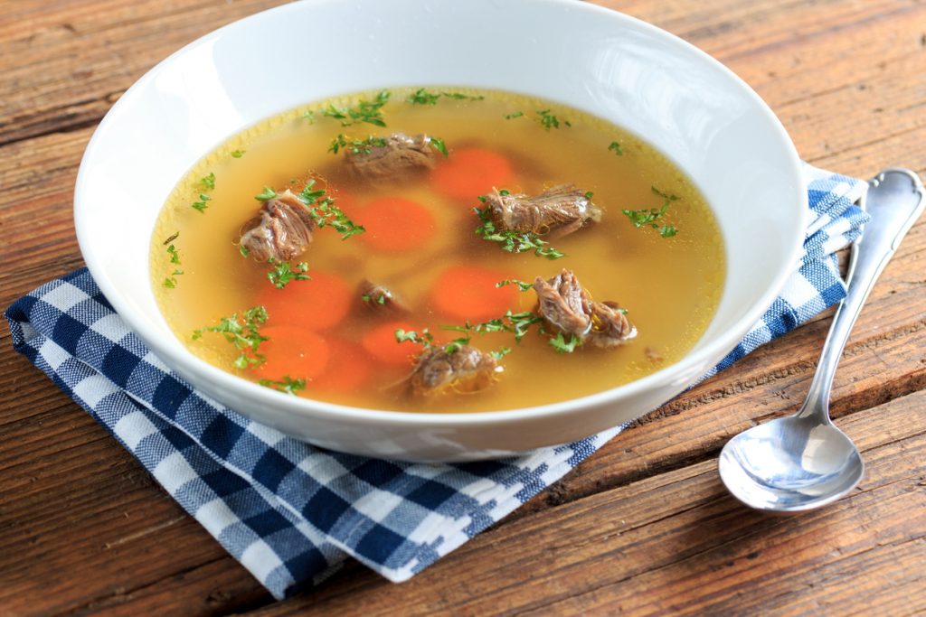 Eine helle Brühe mit Rindfleischstücken und Karottenscheiben ist mit frischer Petersilie bestreut.