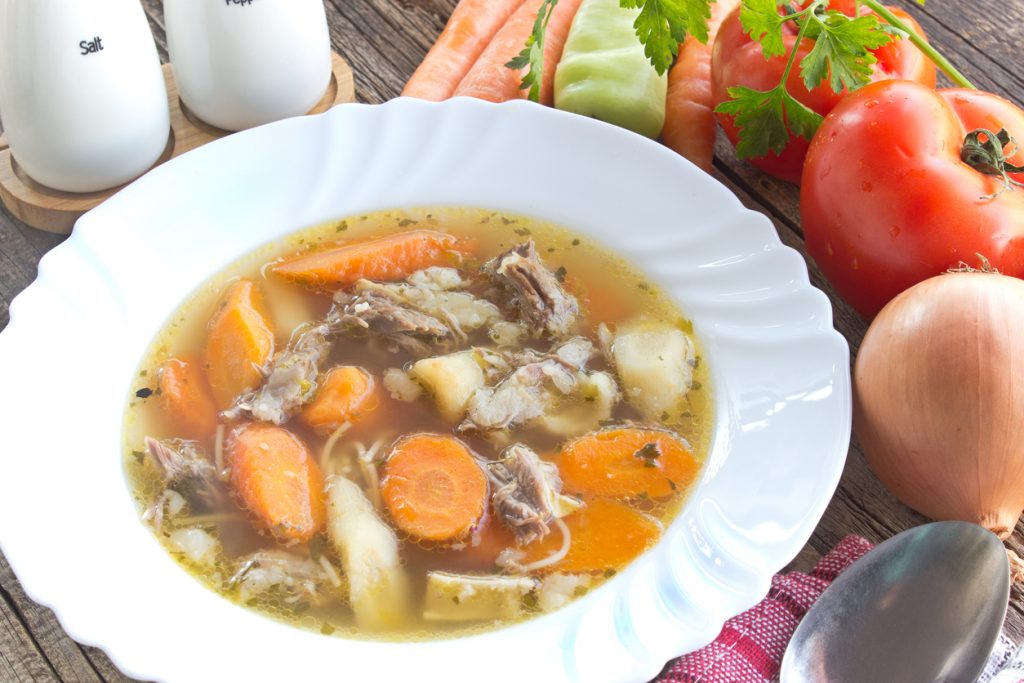Eine dampfende Schüssel Suppe mit Rindfleisch und Karotten ist von Salz- und Pfefferstreuern flankiert.