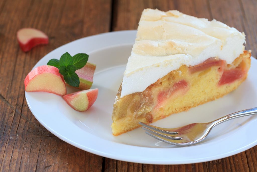 Die Makroaufnahme eines Stücks Rhabarberkuchen zeigt die feine, wolkenartige Struktur des Baisers und die saftigen Rhabarberstücke im Teig.